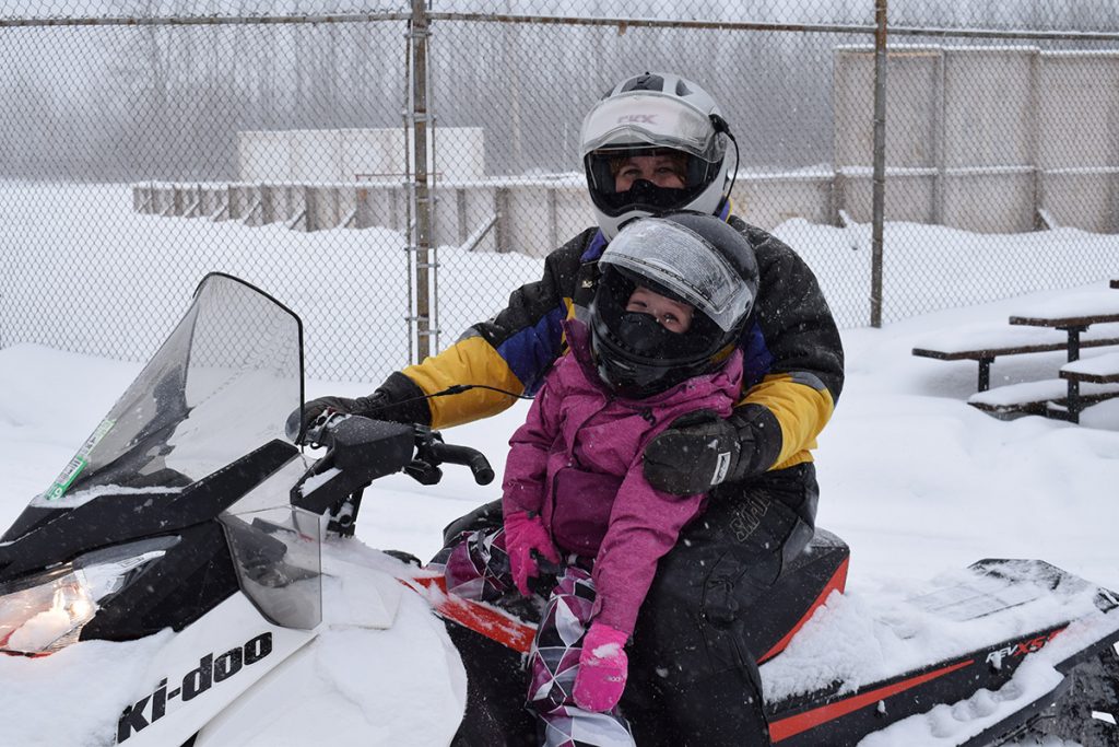 A rider and a little girl on a snowmobile